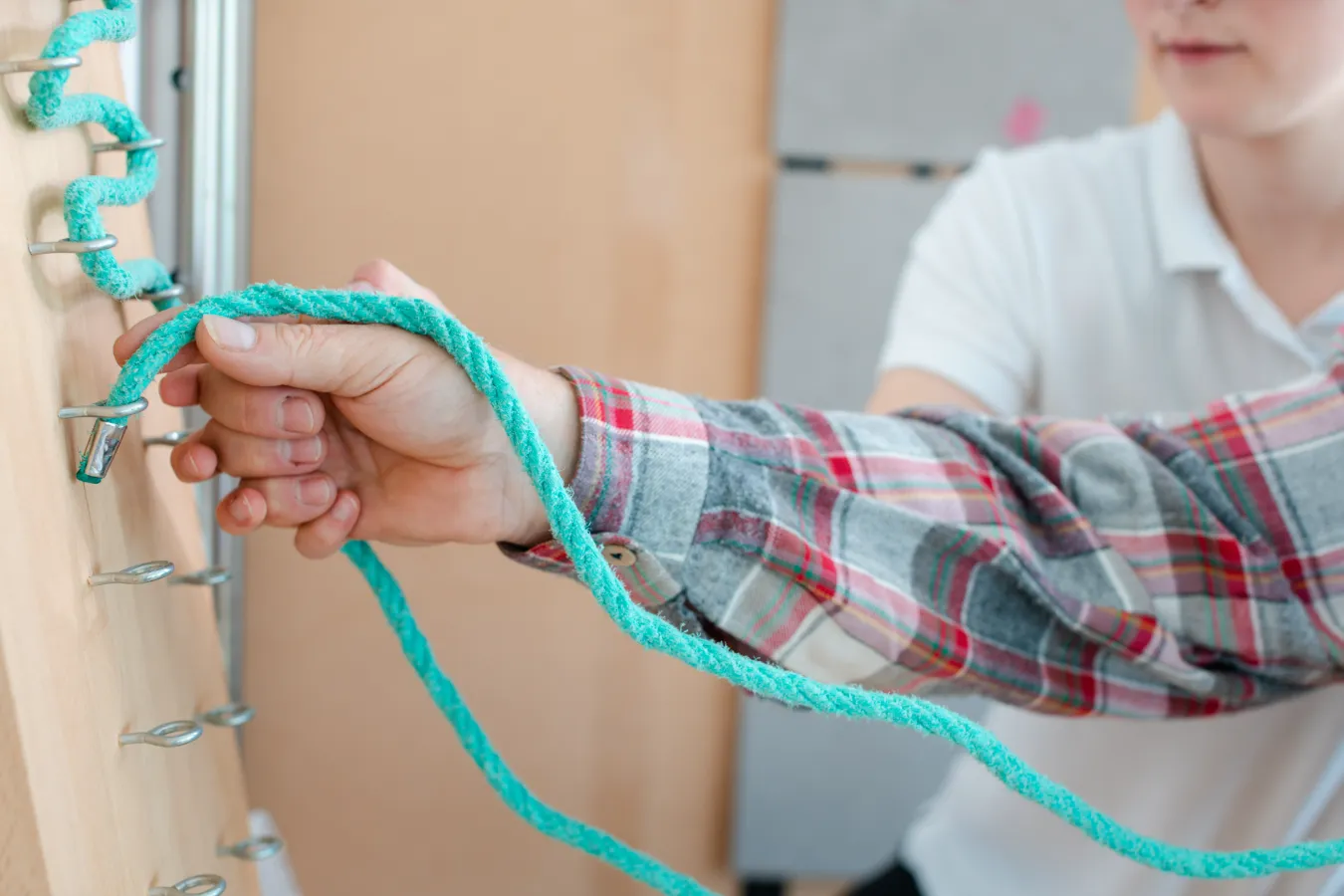 A medical professional assisting a patient putting a rope through hooks for occupational therapy on their hands